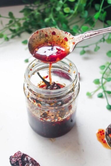 Hot honey drizzling from a silver spoon into a glass jar.