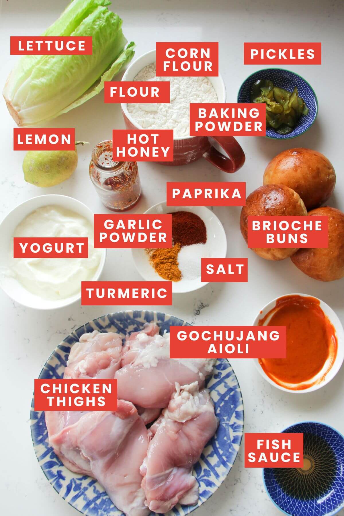 Ingredient for hot honey fried chicken sandwich laid out on a white marble background and labelled.