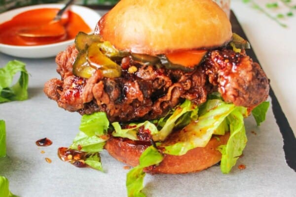 Hot honey fried chicken sandwich on a dark wooden board with small bowl of gochujang aioli in the background.