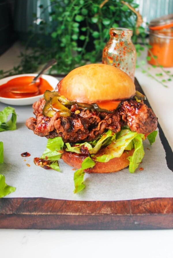 Hot honey fried chicken sandwich on a dark wooden board with small bowl of gochujang aioli in the background.