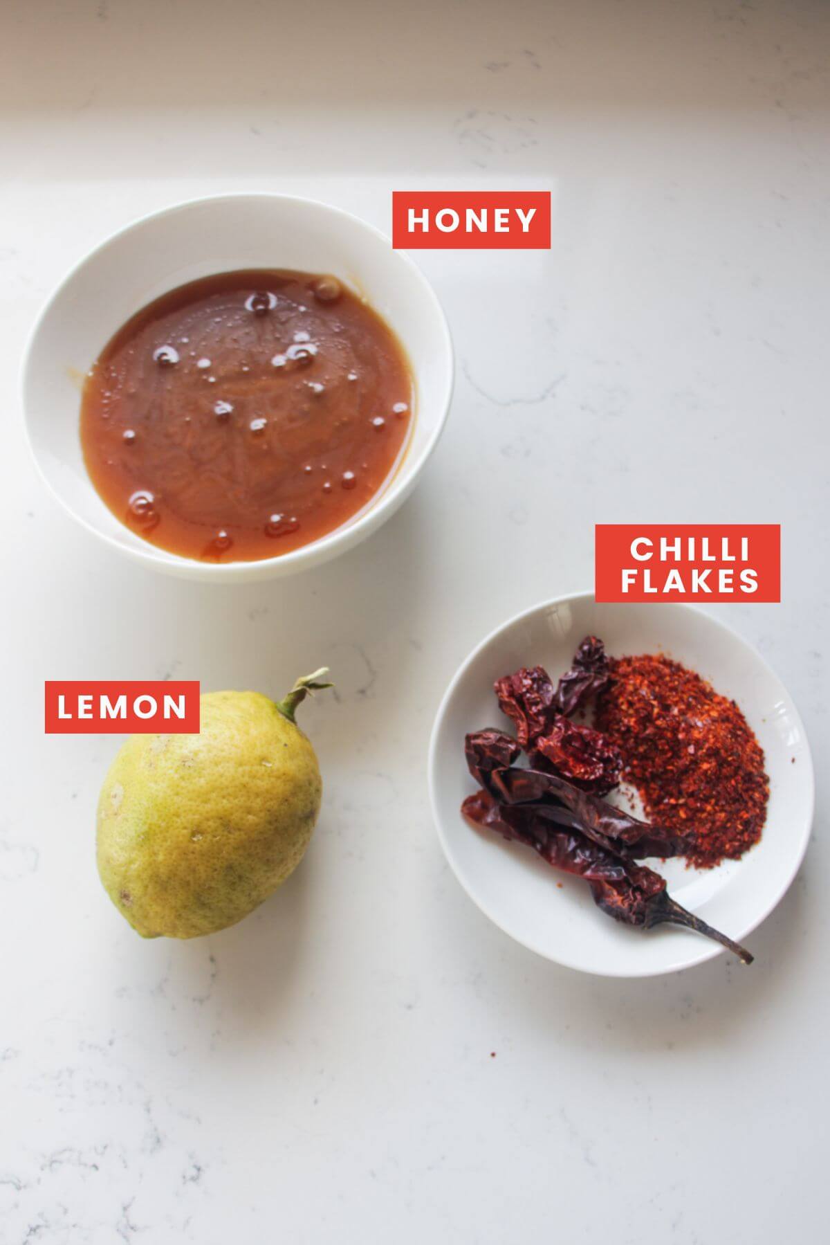 Ingredient for hot honey laid out on a white marble background.