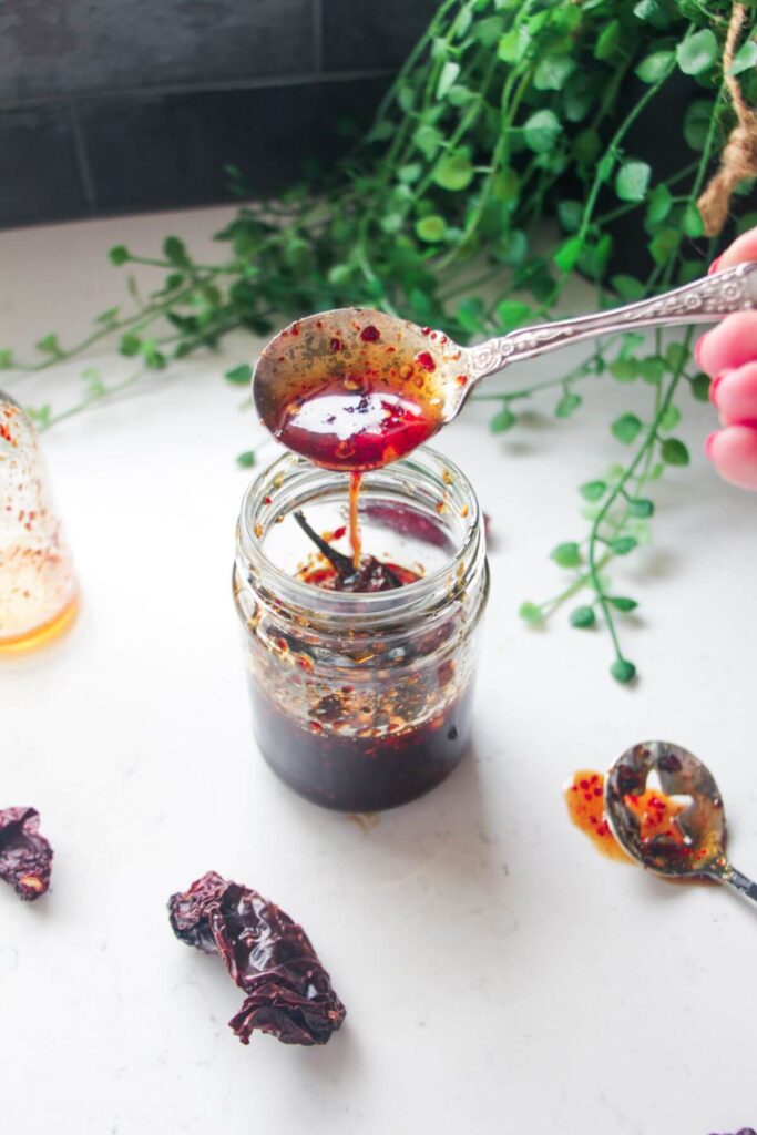 Hot honey drizzling from a silver spoon into a glass jar.