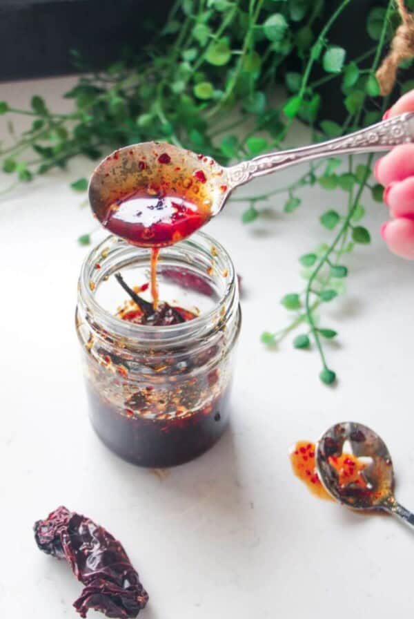 Hot honey drizzling from a silver spoon into a glass jar.