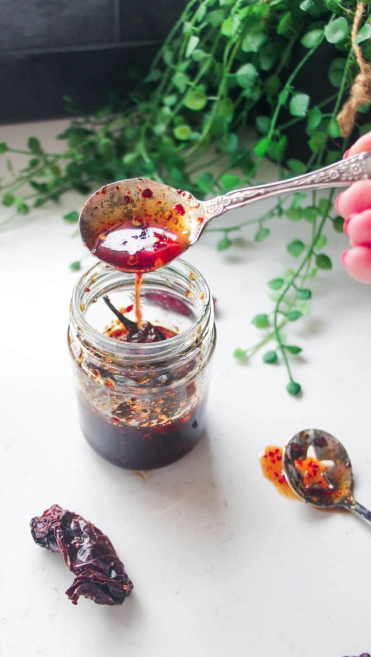 Hot honey drizzling from a silver spoon into a glass jar.