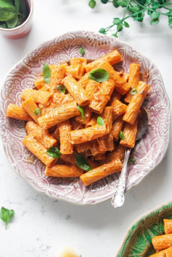 Spicy rigatoni on a pink plate with another small plate of rigatoni next to it.