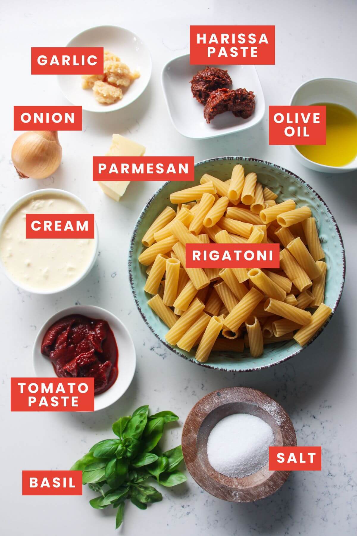 Spicy rigatoni ingredients laid out on a white marble background and labelled.