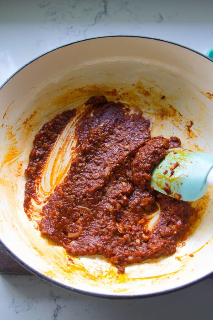 Stirring tomato paste and harissa paste in a large white skillet.