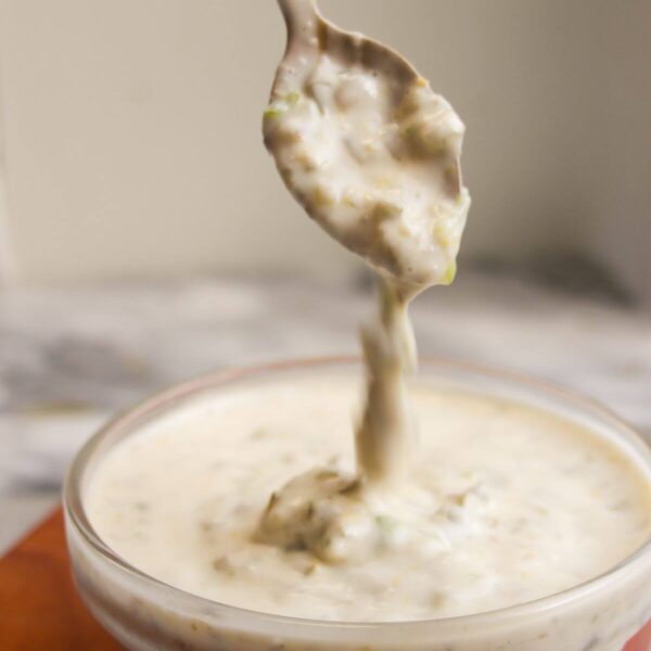 Tartare sauce dripping off a small spoon into a glass bowl.