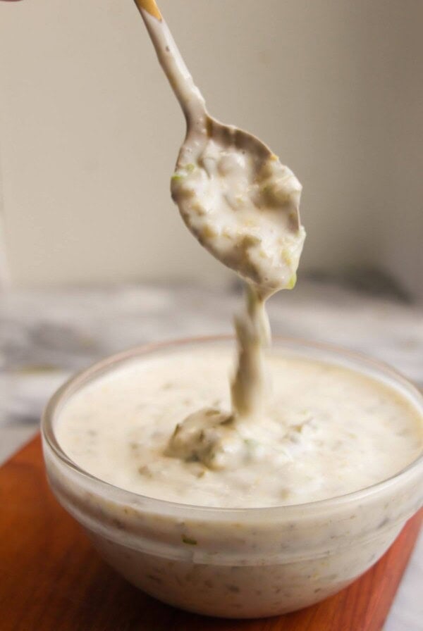 Tartare sauce dripping off a small spoon into a glass bowl.
