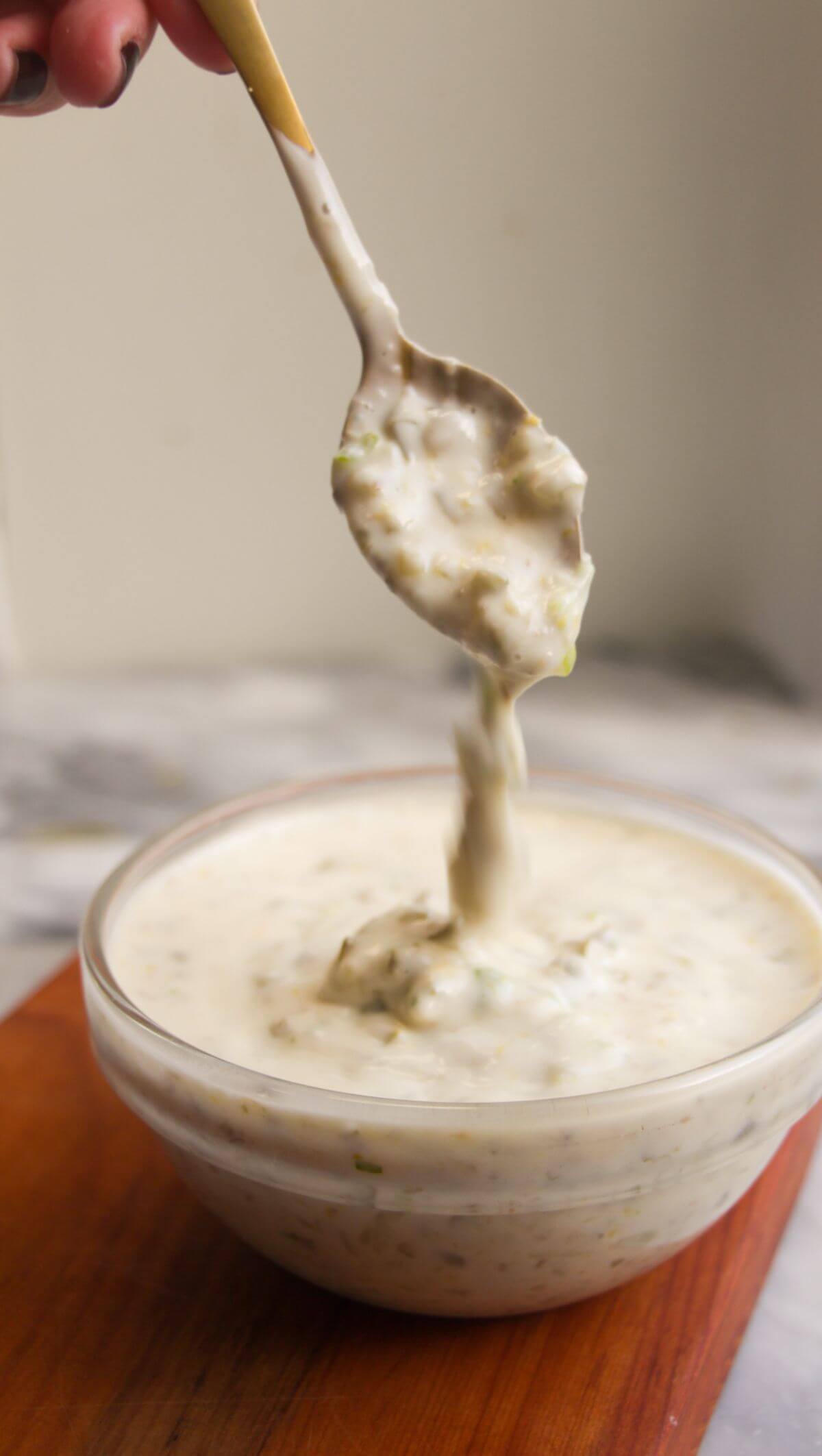 Tartare sauce dripping off a small spoon into a glass bowl.