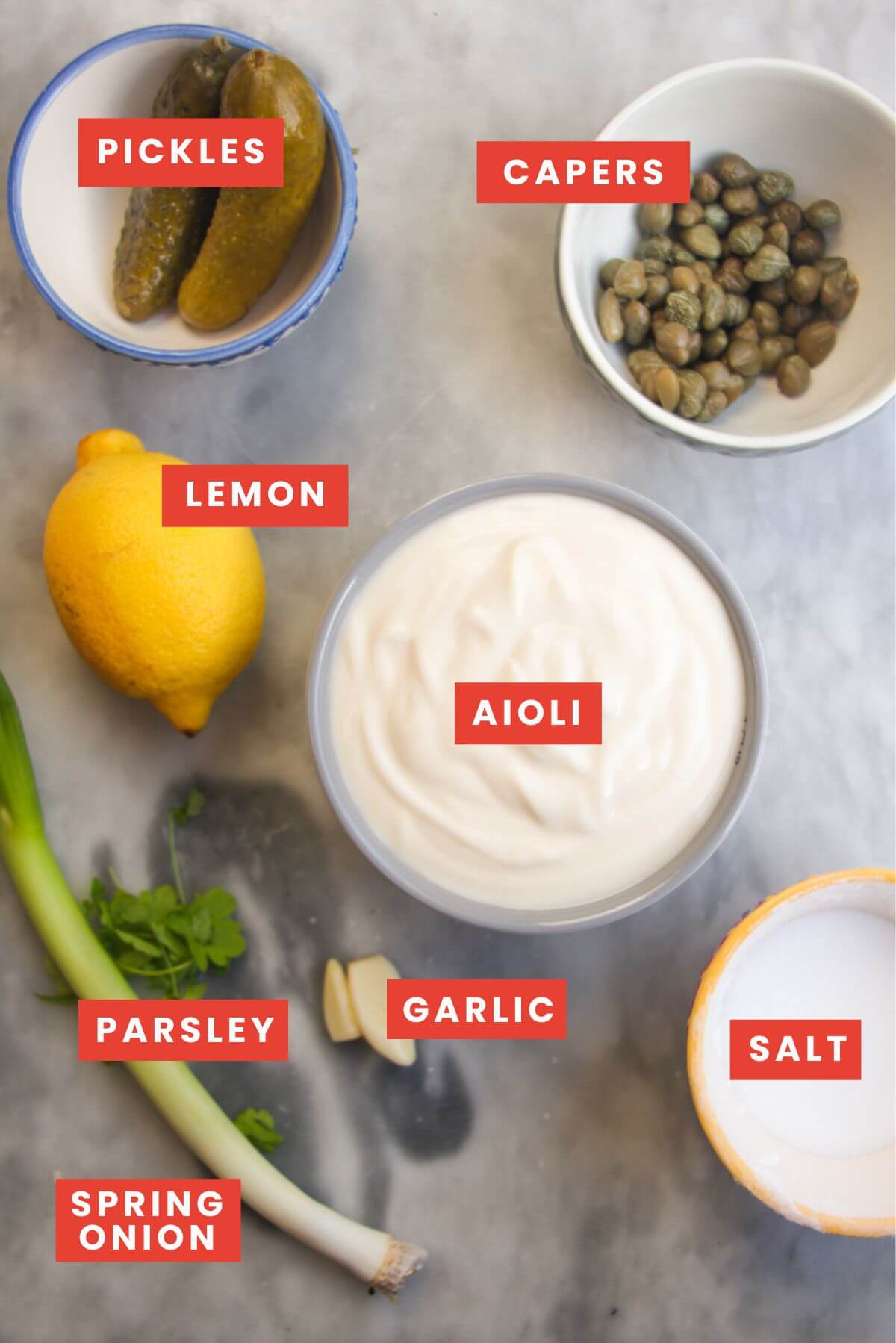 Tartare sauce ingredients laid out on a grey marble background and labelled.