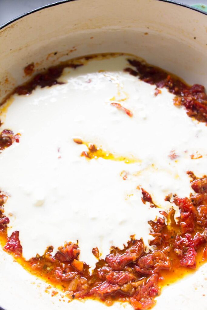 Cream added to sundried tomatoes in a large white skillet.
