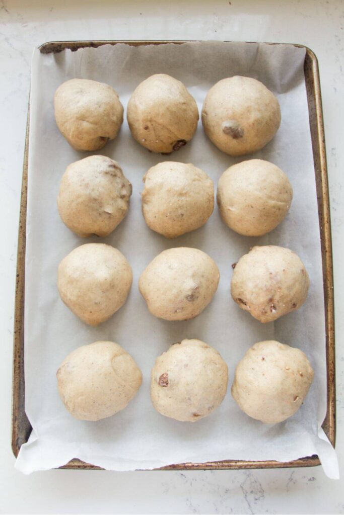 12 mini egg hot cross bun dough balls on a lined oven tray.