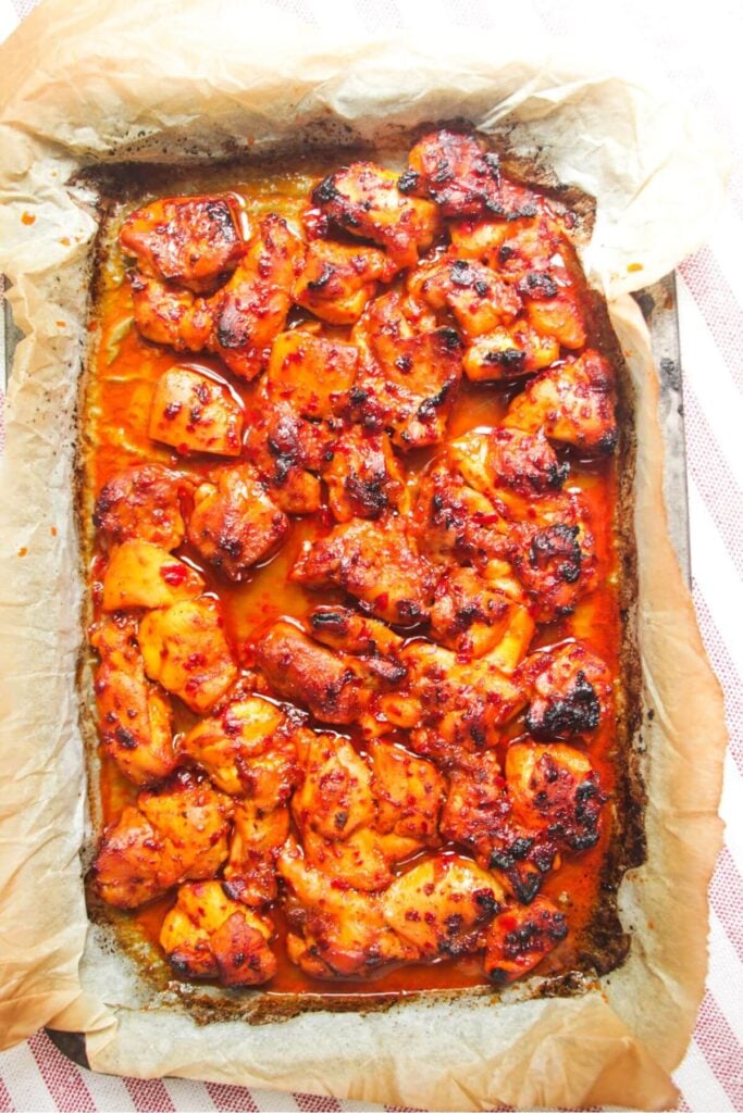 Charred honey harissa chicken in an oven tray.
