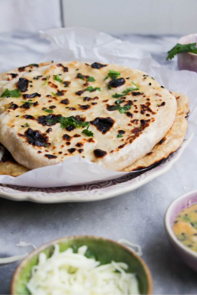 Close up of cheese stuffed naan piled on top of eachother on a plate with cheese in a bowl in front.