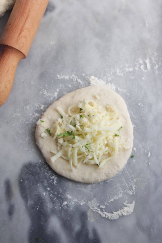 Cheese and herbs piled onto a small circle of dough on a grey marble background.
