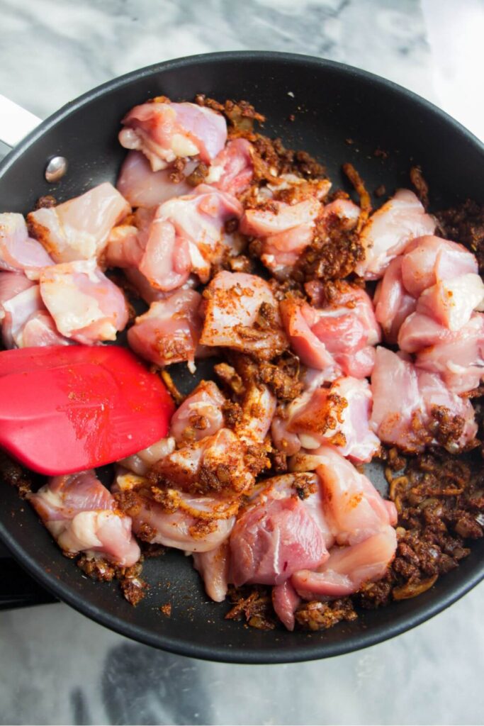 Diced chicken in a small frying pan with spices through it.