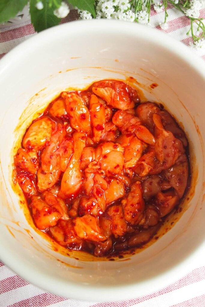 Diced chicken in honey harissa marinade in a bowl.