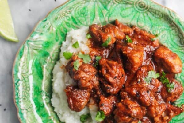 Chicken rogan josh on a bed of white rice on a green plate, with more curry in a small silver dish on the side.