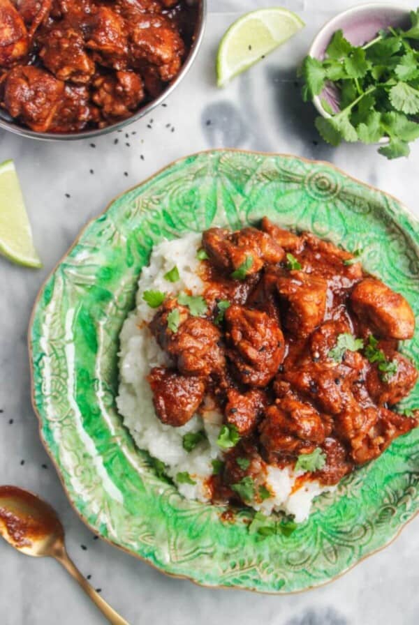 Chicken rogan josh on a bed of white rice on a green plate, with more curry in a small silver dish on the side.