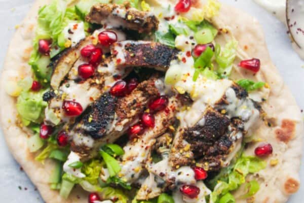 Chicken shawarma wrap on a grey marble background with a small bowl of tahini sauce on the side.