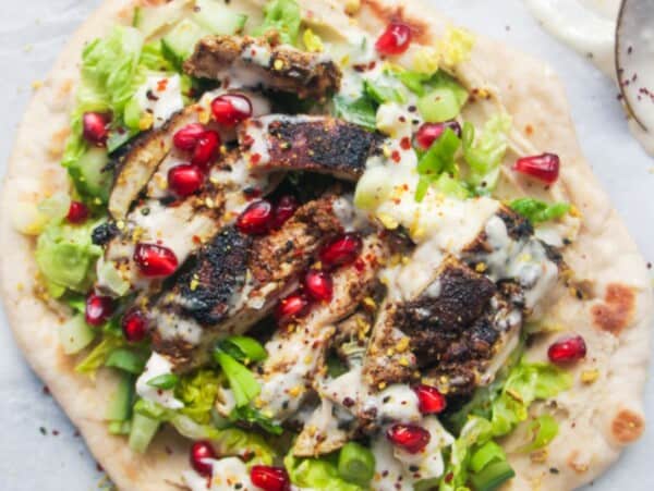 Chicken shawarma wrap on a grey marble background with a small bowl of tahini sauce on the side.