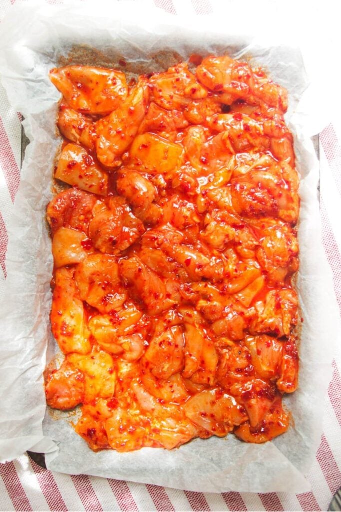 Diced marinated chicken on a lined oven tray.