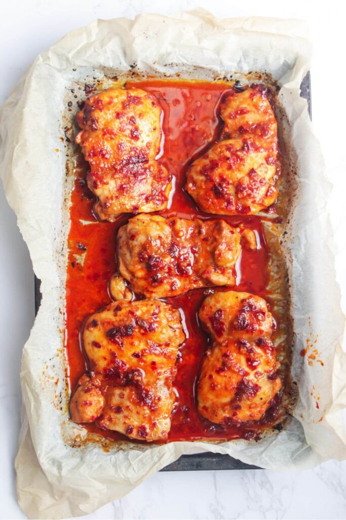 Cooked harissa honey chicken thighs in a lined baking tray.