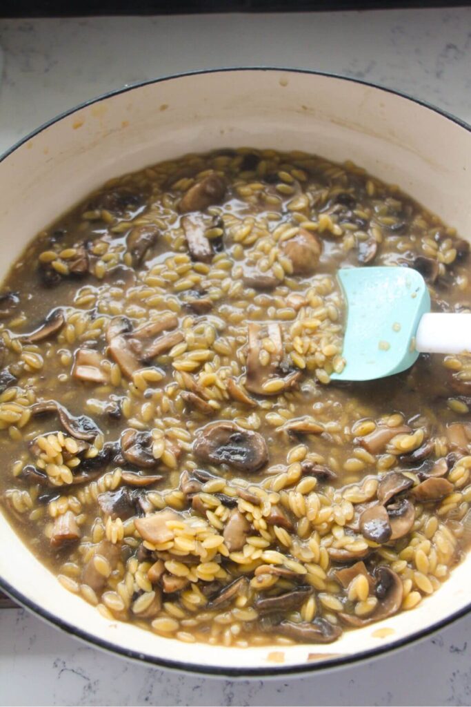 Mushroom orzo being stirred in a large white skillet.