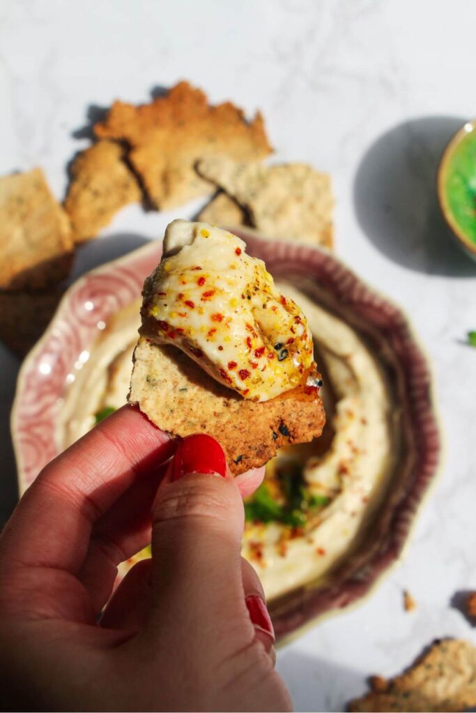 Hand holding up a cracker with white bean dip on it.