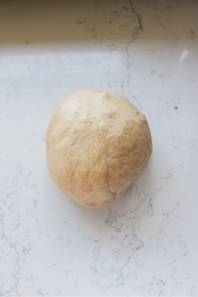 Mini egg hot cross bun dough in a large ball on a white marble background.
