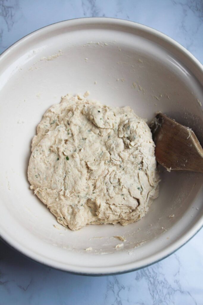 Rough, shaggy rosemary parmesan bread dough in a large white mixing bowl.
