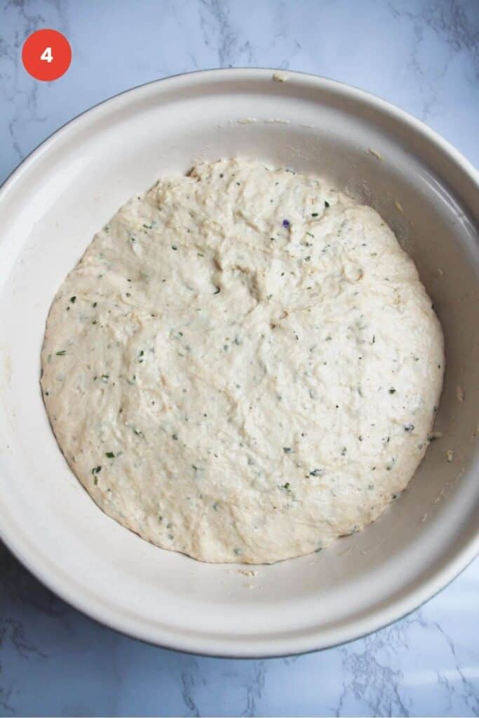 Risen rosemary parmesan bread dough in bowl.