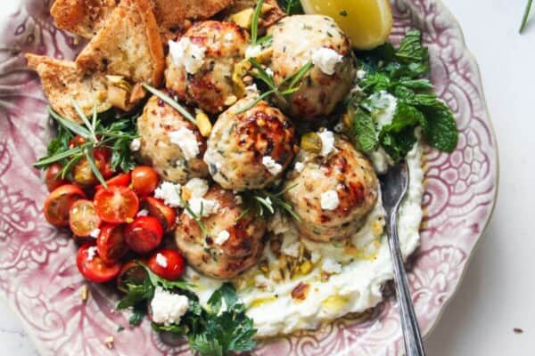 Fresh, zesty, juicy Greek chicken meatballs are a super easy, versatile 20 minute meal. Piled onto quick tzatziki sauce, topped with creamy feta, cherry tomatoes and herbs, they make a wonderful weeknight winner the whole family will love.