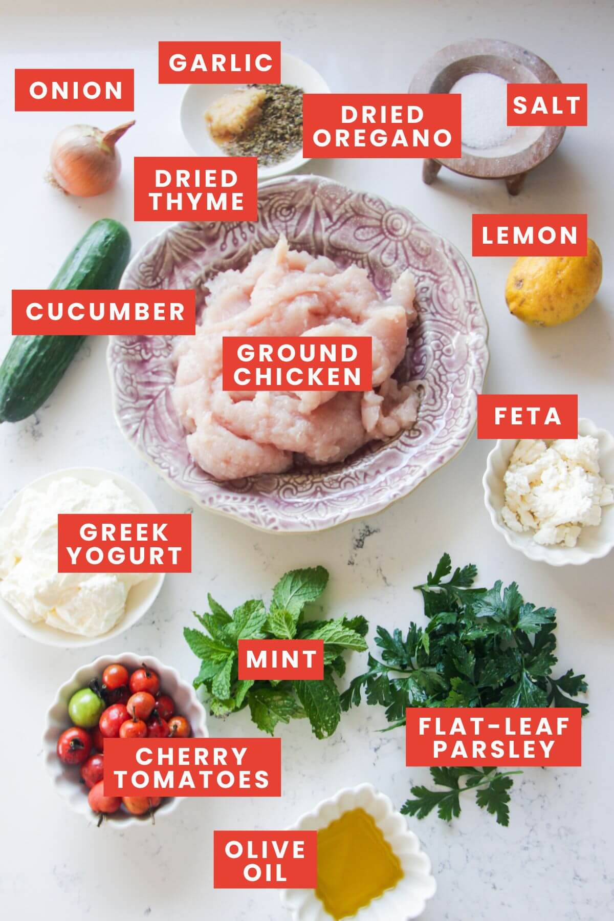 Ingredients for Greek chicken meatballs laid out on a white marble background and labelled.