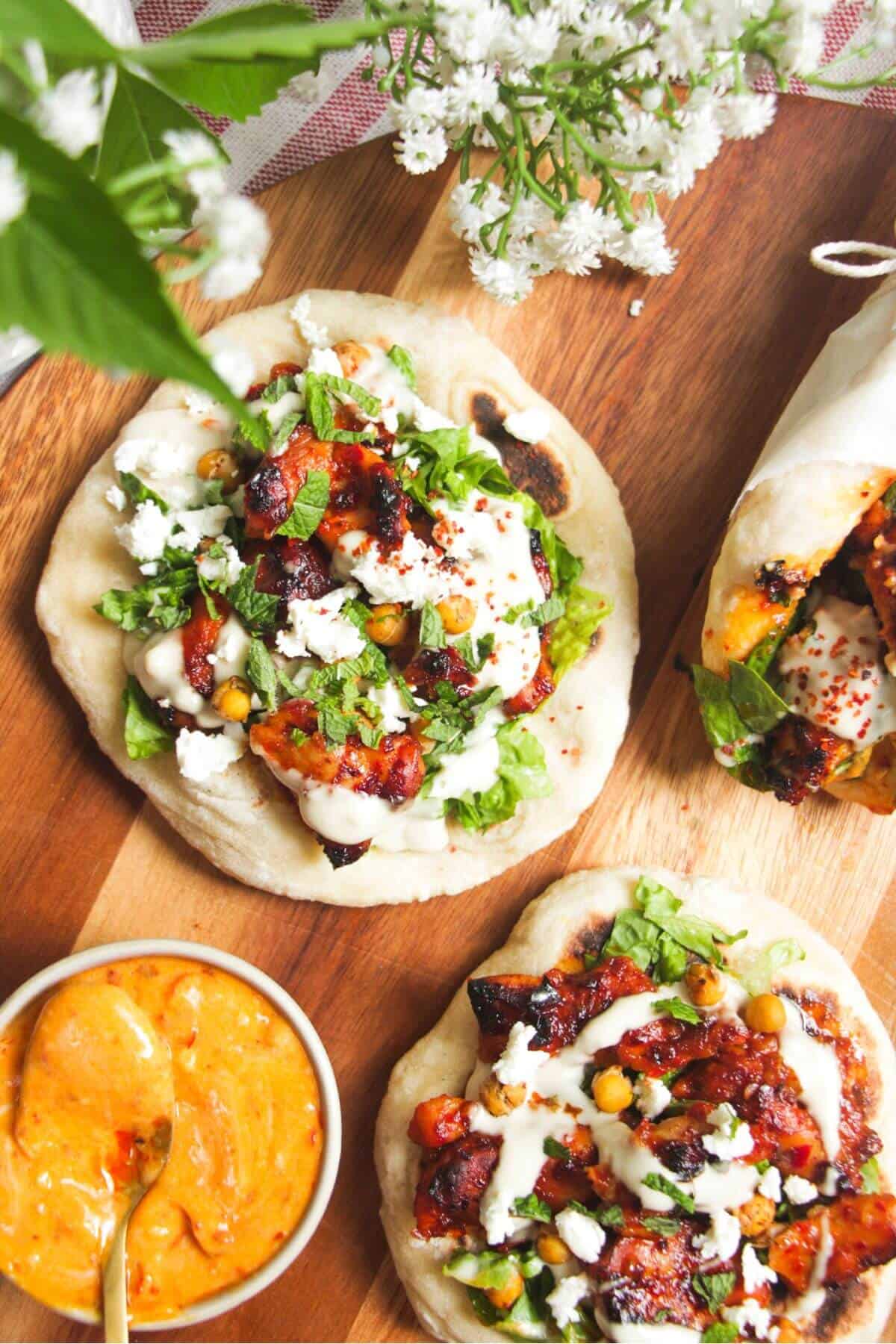 Three flatbreads piled with honey harissa chicken, salad and feta.