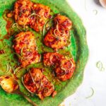 Five harissa honey chicken thighs on a large green serving plate with spring onions on top.