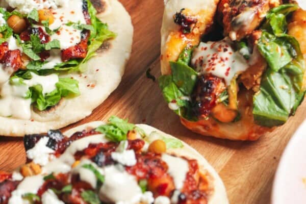 Three flatbreads piled with honey harissa chicken, salad and feta.