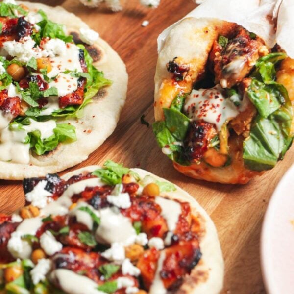 Three flatbreads piled with honey harissa chicken, salad and feta.