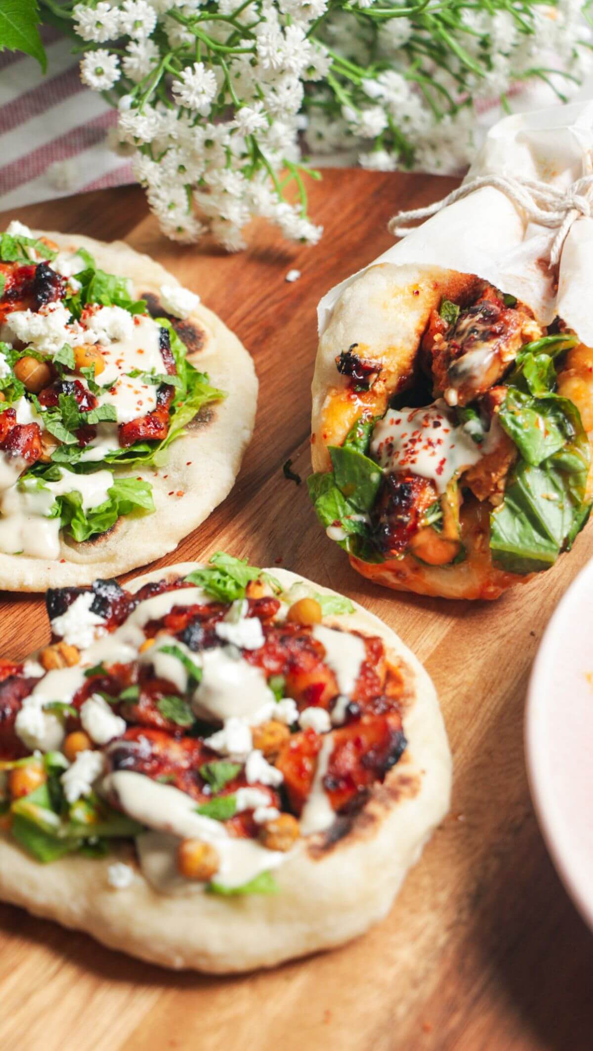 Three flatbreads piled with honey harissa chicken, salad and feta.