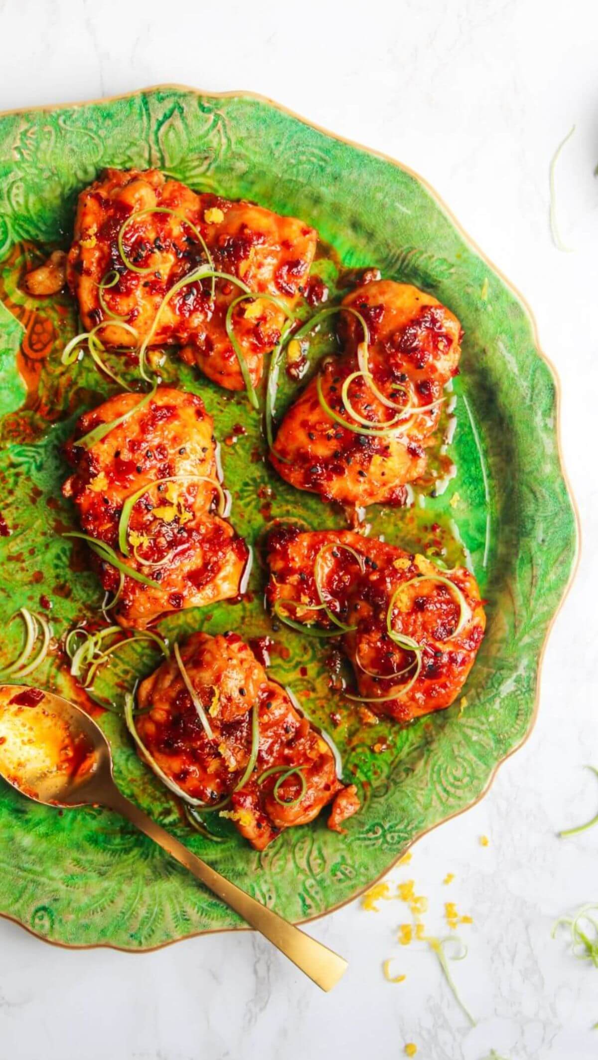 Five harissa honey chicken thighs on a large green serving plate with spring onions on top.