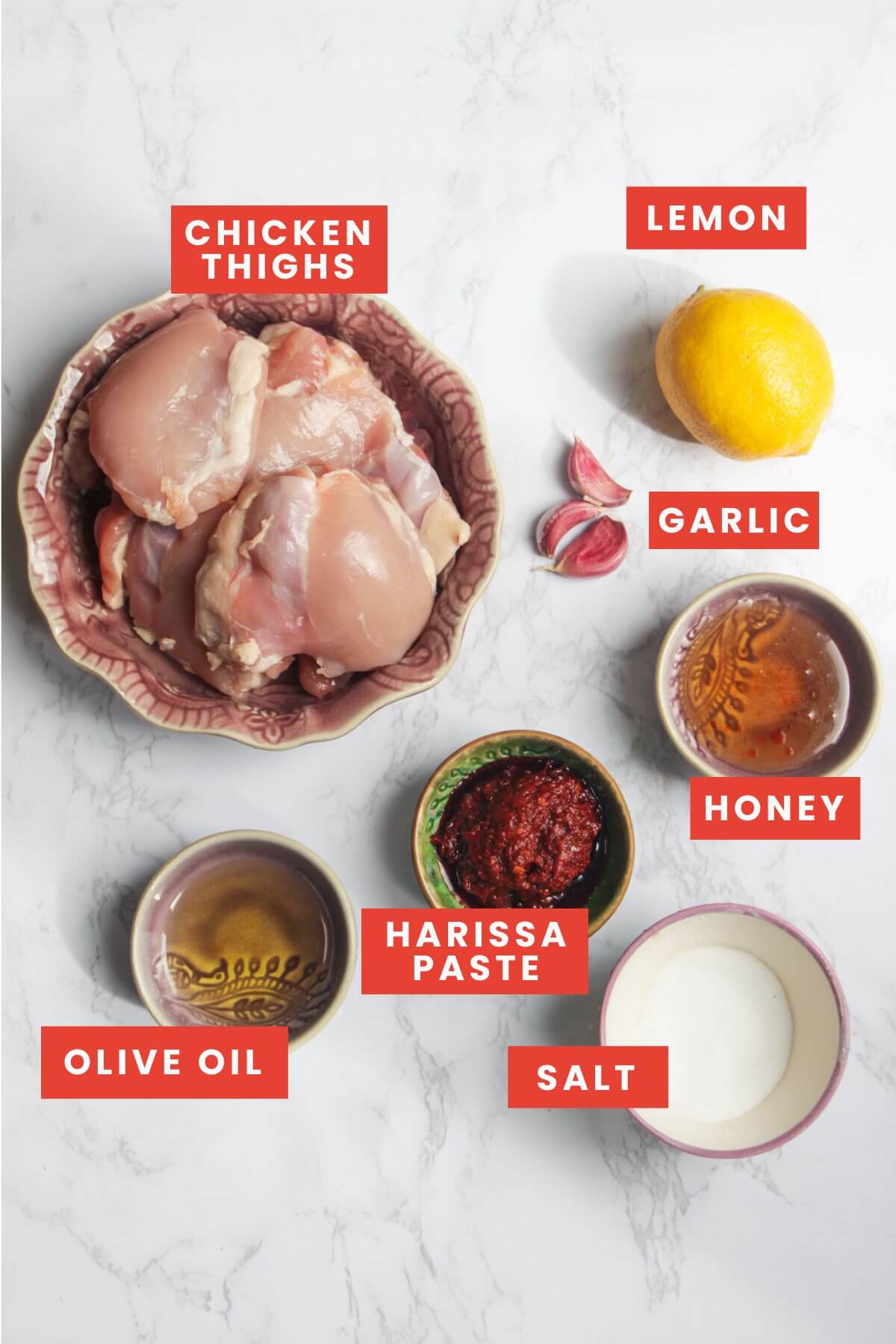 Harissa honey chicken ingredients laid out on a white marble background and labelled.