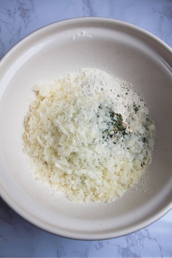 Flour, grated cheese, chopped rosemary, yeast and salt in a large white mixing bowl.