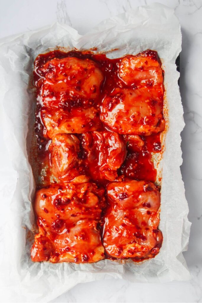 Marinated harissa honey chicken thighs on a lined baking tray.