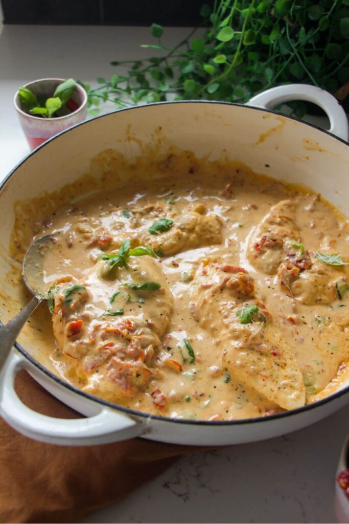 Chicken breasts in creamy sundried tomato sauce in a large white skillet.