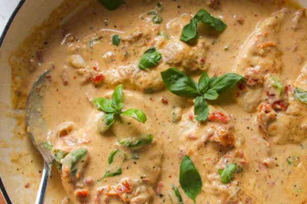 Chicken breasts in creamy sundried tomato sauce in a large white skillet.
