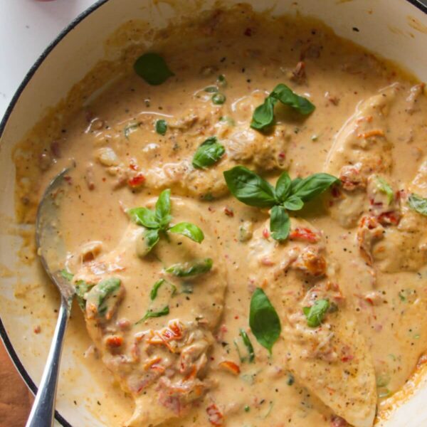 Chicken breasts in creamy sundried tomato sauce in a large white skillet.