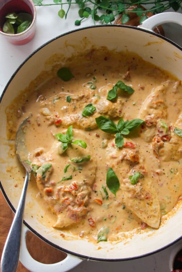 Chicken breasts in creamy sundried tomato sauce in a large white skillet.