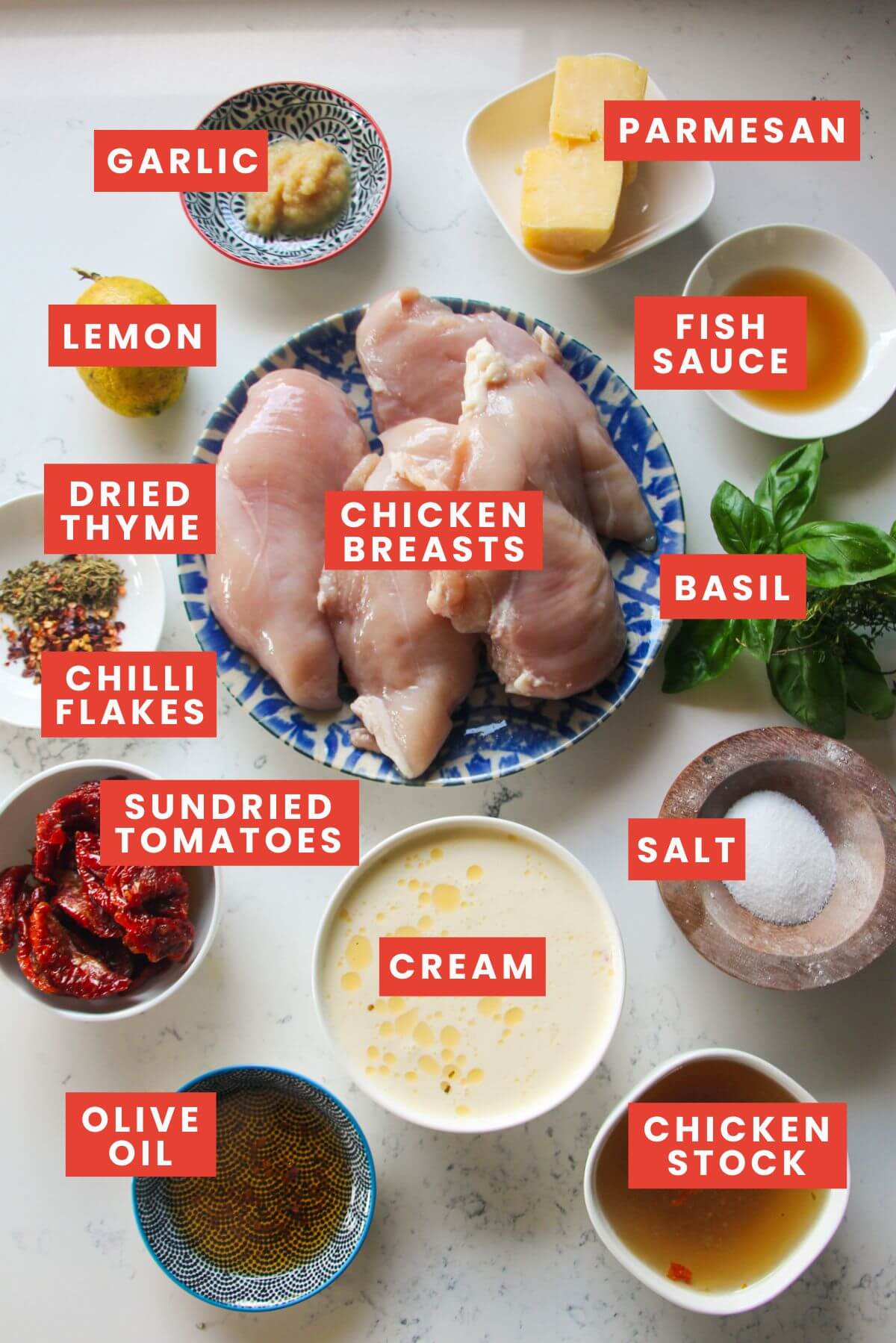 Ingredients for marry me chicken laid out on a white marble background and labelled.