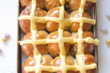 12 mini egg chocolate hot cross buns in a lined oven tray with more mini eggs on the side.